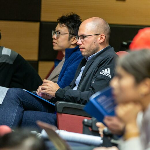 man wearing black adidas jacket sitting on chair near another man wearing blue jacket