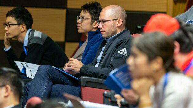 man wearing black adidas jacket sitting on chair near another man wearing blue jacket